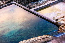 Load image into Gallery viewer, A photograph featuring the serene bluepool  and rocks, located on south coast NSW with a warm glow from sunrise. 